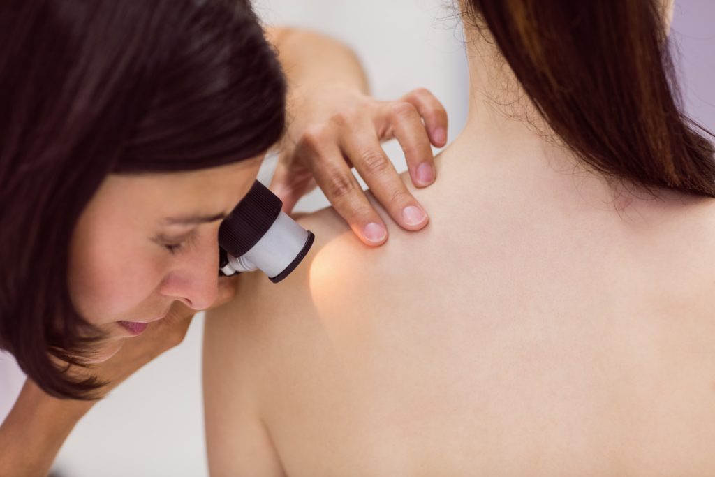 A dermatologist examines a patient's skin through a dermatoscope.